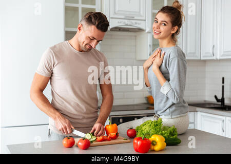 Ritratto di una bella coppia amorevole insalata di cottura insieme mentre in piedi su una cucina a casa, uomo taglio di vegetali Foto Stock