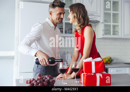 Giovane Uomo in camicia bianca versando il vino in bicchieri e guardando la sua donna gorgeous in abito rosso per San Valentino Foto Stock