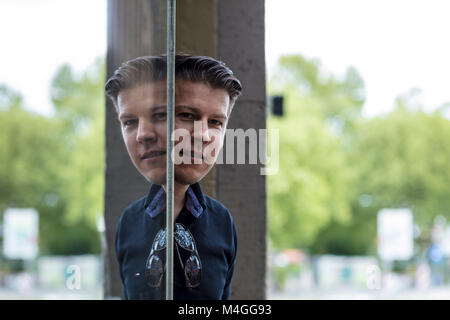 Uomo in posa nella parte anteriore della finestra di vetro che riflette la sua immagine. Close up. Foto Stock