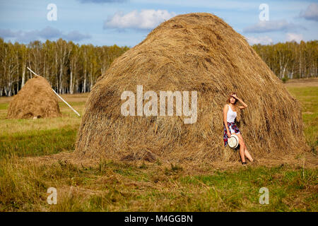 Giovane biondo country girl in hat vicino haystacks Foto Stock