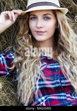 Giovane biondo con gli occhi azzurri paese sorridente ragazza in hat sedersi vicino a haystacks Foto Stock