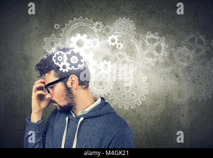 Considerato giovane uomo alla ricerca di una soluzione con meccanismi a ingranaggi sopra la sua testa Foto Stock