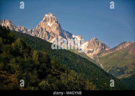 I picchi di maggiore Svaneti, Georgia, contro il cielo blu e il verde delle colline Foto Stock