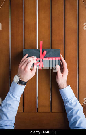 Immagine ritagliata dell uomo la legatura nastro rosso sul presente box Foto Stock