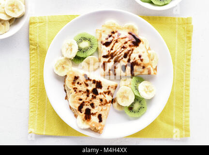Crepes con banana, fette di kiwi e salsa al cioccolato. Vista superiore, laici piatta Foto Stock