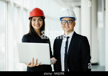 Gli ingegneri che lavorano su un sito di costruzione in possesso di un computer portatile, architetto uomo al lavoro con la donna ingegnere ispezione nei luoghi di lavoro per il progetto architettonico Foto Stock