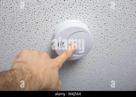 Basso angolo vista di una persona mano, premendo il rilevatore di fumo sul soffitto Foto Stock