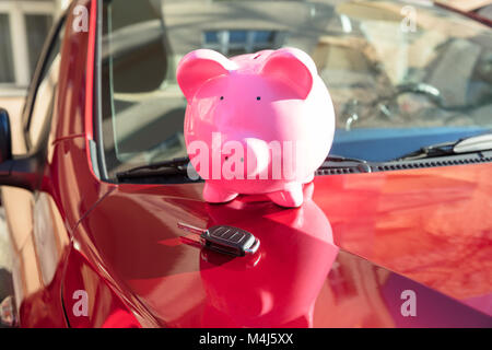 Close-up di un Piggybank con chiave auto sulla nuova auto rossa Foto Stock