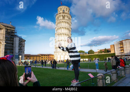 Pisa, Italia - 11 Febbraio 2018: una ragazza in posa per una foto con la famosa Torre di Pisa in background, in Piazza dei Miracoli. Foto Stock