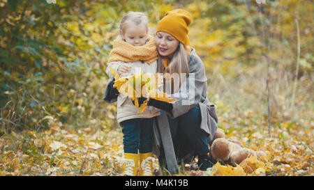 La bionda bambina con la sua mamma passeggiate nel parco di autunno - sono divertenti e raccogliere foglie, close up Foto Stock