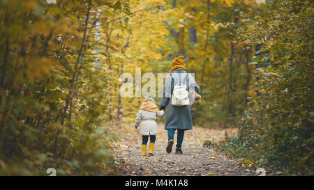 Gioiosa bambina con la sua mamma e Teddy Bear passeggiate nel parco di autunno, vista posteriore Foto Stock