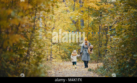 Bella bionda bambina con la sua mamma passeggiate nel parco di autunno - sono divertenti e raccogliere foglie Foto Stock