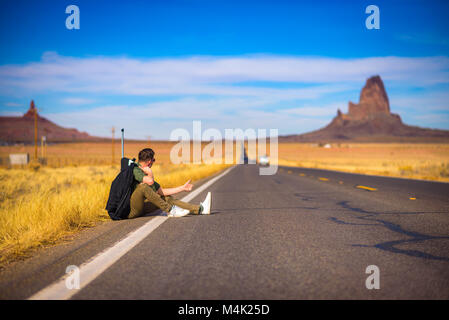 Stanco sollevatore-escursionista con la valigia seduto su una strada Foto Stock