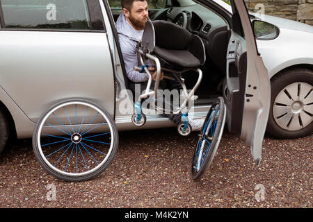 Uomo disabili su sedia a rotelle di contenimento mentre l'imbarco nella sua auto Foto Stock