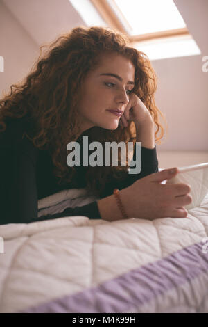 Donna che utilizza digitale compressa mentre giaceva sul letto in camera da letto Foto Stock
