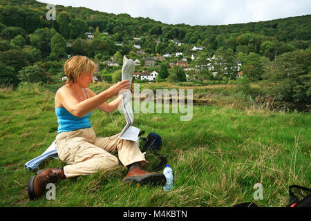 Donna in appoggio sulle rive del fiume Wye vicino Brockweir mappa di lettura mentre passeggiate da Chepstow a Prestatyn su Offa's Dyke lunga distanza sentiero Foto Stock