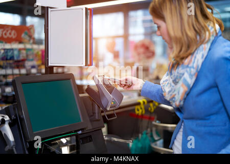 Giovane donna fare self-checkout nel supermercato con telefono mobile Foto Stock