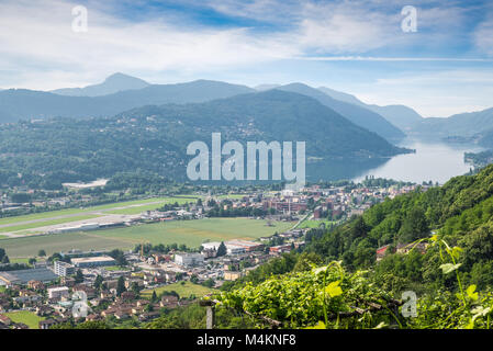Il lago di Lugano, Svizzera. Pittoresca veduta aerea della città di Agno, il lago di Lugano, Lugano Airport su un bel giorno di estate Foto Stock