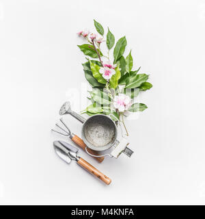 Annaffiatoio con utensili da giardinaggio e verde mazzo di ramoscelli con decorazione fiore bianco su sfondo scrivania, vista dall'alto Foto Stock