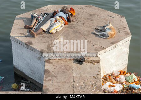 Un uomo con una gamba dorme al sole accanto ad un cane. Varanasi, India. Foto Stock