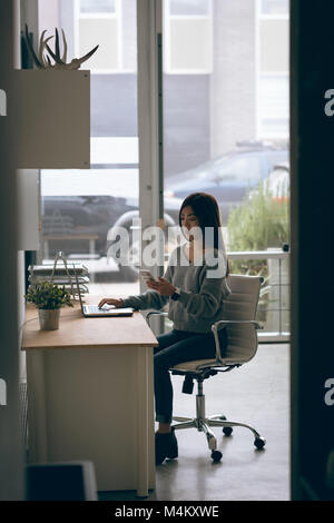 Executive femmina utilizzando il telefono cellulare mentre si lavora sul computer portatile alla reception Foto Stock