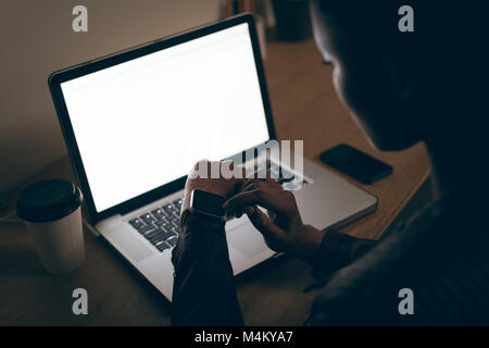 Executive femmina utilizzando smartwatch mentre si lavora sul computer portatile alla reception Foto Stock