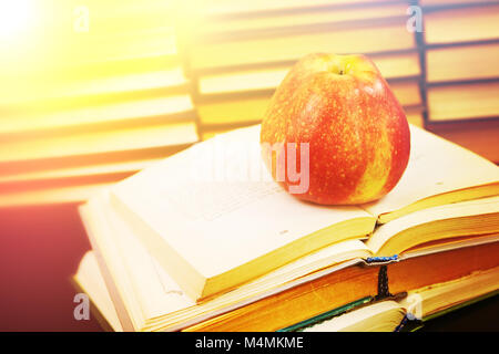 Red apple sul libro aperto contro lo sfondo di una pila di libri Foto Stock