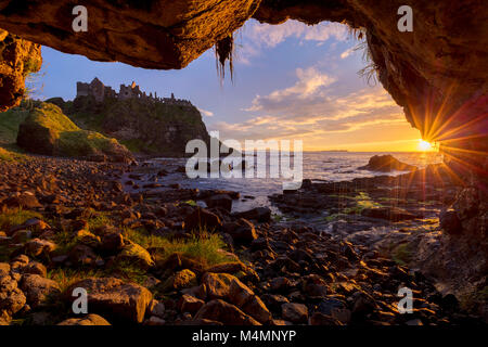 Sunset over Dunluce Castle dall'interno di una grotta marina. La Causeway Coast, County Antrim, Irlanda del Nord. Foto Stock