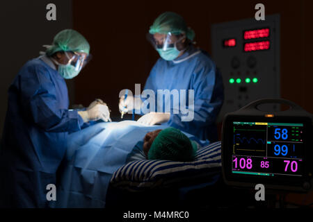 Elettrocardiogramma in ospedale chirurgia di emergenza operativo camera mostra frequenza cardiaca del paziente con blur equipe di chirurghi in background. Salute e medicin Foto Stock