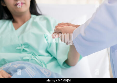 Gentile uomo medico mani tenendo la mano del paziente seduto alla scrivania di incoraggiamento, empatia, tifo e supporto durante la visita medica. Bad nuovo Foto Stock