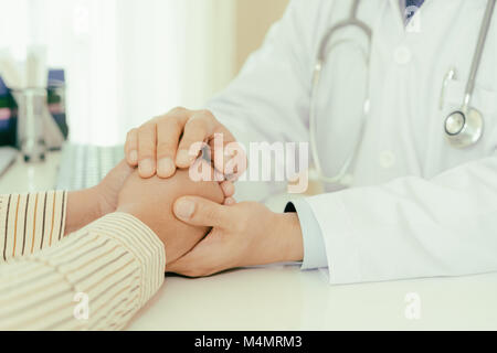 Gentile uomo medico mani tenendo la mano del paziente seduto alla scrivania di incoraggiamento, empatia, tifo e supporto durante la visita medica. Bad nuovo Foto Stock