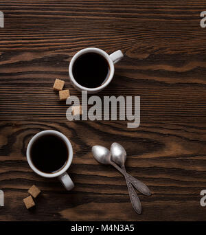 Due tazze di caffè espresso con pezzi di zucchero di canna su un tavolo di legno. Foto Stock