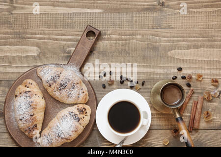 Tre deliziosi croissant appena sfornati e la tazza di caffè sulla tavola di legno. Vista dall'alto. Concetto di colazione. Foto Stock