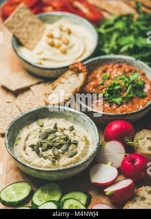 Vegano scheda snack. Varie salse vegetariano hummus, babaganush e muhammara con cracker, pane e verdure fresche, sullo sfondo di legno. Pulire mangiare Foto Stock