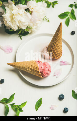 Rosa fragola e cocco gelato scoop, dolce coni e peonie bouquet di fiori sulla piastra su sfondo bianco. In estate il concetto di cibo Foto Stock