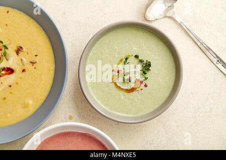 Flatlay con tre ciotole con colorati vegetariano zuppe cremose con broccoli, zucca e barbabietola guarnito con semi di zucca e olio d'oliva sul beige Foto Stock