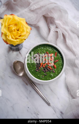 Frullato di verde e rabboccato con goji bacche e pennini di cacao in un bianco vaso in ceramica Foto Stock