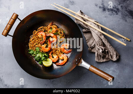 Ramen friggere gli spaghetti con i gamberi in padella wok sul cemento grigio sfondo Foto Stock