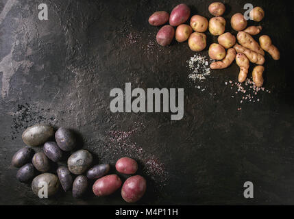 Varietà di materie organiche non cotte patate diversi tipi e colori rosso, giallo e viola con vari di sale più scuro dello sfondo texture. Vista superiore, co Foto Stock