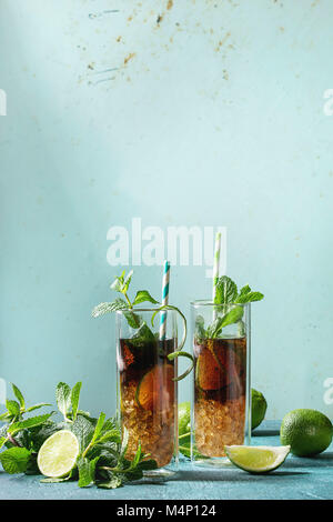 Due bicchieri di classic cuba libre cocktail con calce, menta, ghiaccio tritato e cola, servita con gli ingredienti di cui sopra e cocktail retrò tubi su turquois Foto Stock