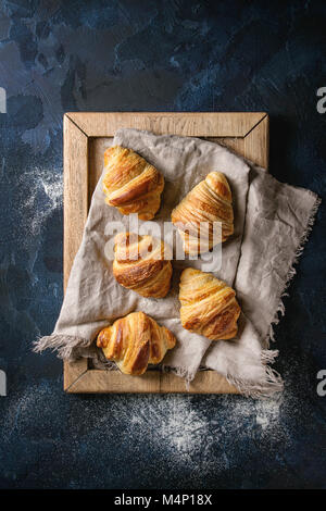 Freschi di forno cornetti tradizionali su lino tessile vassoio in legno su blu scuro dello sfondo texture. Vista superiore, spazio Foto Stock