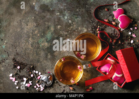 L'amore il giorno di San Valentino biglietto di auguri con due bicchieri di tè caldo, boccioli di rosa, forma di cuore biscotti fatti in casa come dono, rosa zucchero, filtro di tè rosso e ribbo Foto Stock