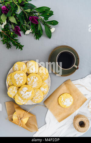 I cookie di limone impilati su una piastra fotografata da vista dall'alto. Bianco e fiori viola, un cookie su un pezzo di carta marrone, alcuni cookie avvolto in b Foto Stock