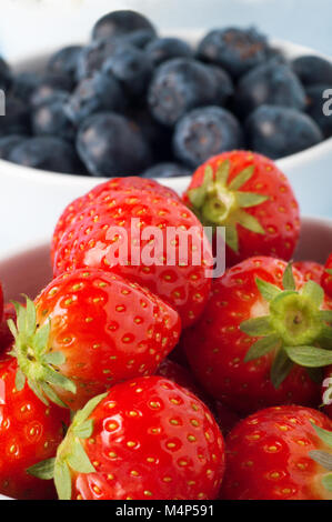 Close up di fragole un riempimento bianco vaso in ceramica con mirtilli nella messa a fuoco morbida dello sfondo. Foto Stock