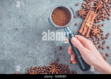 Barista mano che tiene un portafilter con caffè macinato. Immagine di intestazione con i chicchi di caffè. Vista dall'alto. Foto Stock