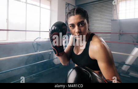 Boxer femmina di mettere in pratica le sue mosse all'interno di un boxing studio. Close up di un boxer femmina facendo shadow boxing all'interno di un anello di inscatolamento. Foto Stock