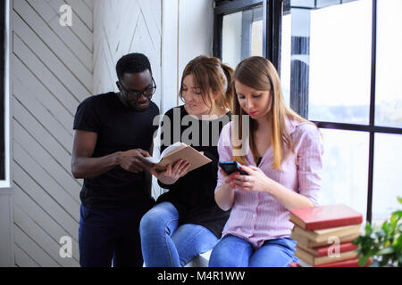 Un uomo nero e due ragazze la lettura di un libro. Foto Stock