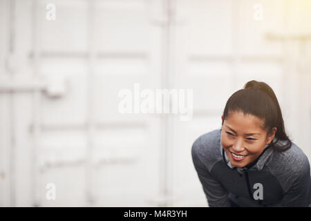 Montare la giovane donna asiatica in sportswear sorridere mentre prendendo una pausa dall'esterno Foto Stock