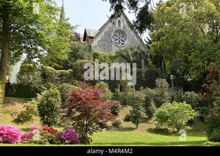 Una bella e antica chiesa in un giardino ricco di alberi e fiori e verde nel lago di Como, Italia Foto Stock