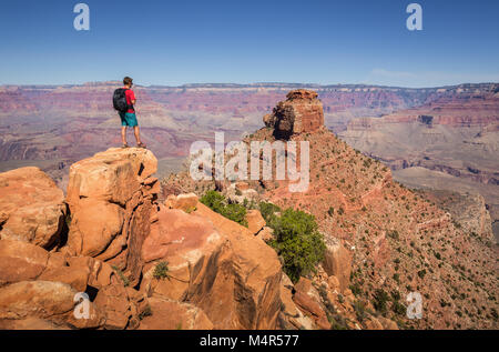 Un giovane maschio escursionista è in piedi su una roccia a sud di Kaibab Trail godendo della splendida vista sul famoso Grand Canyon in una giornata di sole, Arizona, Stati Uniti d'America Foto Stock